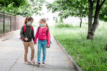 Obraz premium Two little schoolgirls going back to school during covid-19 pandemic. School child wearing protective face mask in school.