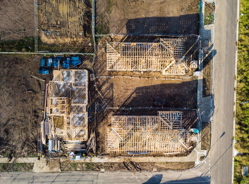 An aerial view of three houses on a corner during the frame stage of construction, almost like a race to be completed each house reveals its differences as they get completed.