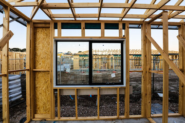 Views of another house being constructed through double glazed windows that are installed in the house frame. This is an early stage of house construction before plumbing or electrical is even run.