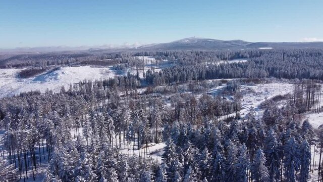 Drone flight over snow-covered forest in the Harz mountains, Lower Saxony, Germany. Clear blue sky on a cold winter day. In the distance Mount Brocken in Saxony-Anhalt.