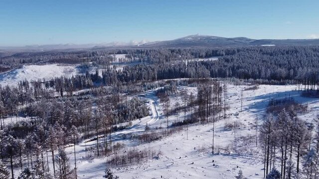 Drone flight over snow-covered forest in the Harz mountains, Lower Saxony, Germany. Clear blue sky on a cold winter day. In the distance Mount Brocken in Saxony-Anhalt.