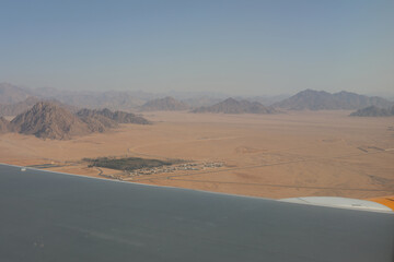 Fototapeta na wymiar Aerial view of desert mountains from the window of plane. Travel to African continent. Landing in Sharm El Sheikh resort in the sunny hot Africa. View of highway in the desert.