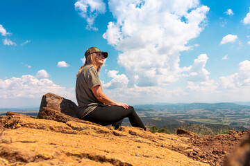 Tourist girl hiker resting at the top of the mountain and enjoying amazing landscape view of mountains and beautiful sky