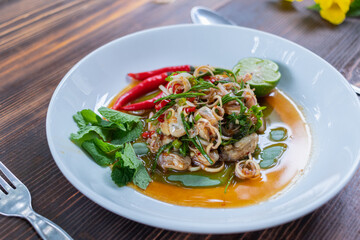 Fresh oysters are served in a white plate and topped with a spicy Thai-style sauce, also known as 