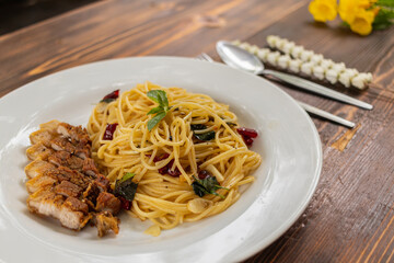 Thai-style stir-fried spaghetti with dried chilli sauce and hot, tender and delicious pork cutlets are served in a white plate on a wooden table, resulting in a spicy spaghetti and fragrant pork cutle