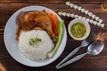 Roasted chicken thighs and drumsticks are served with jasmine rice and fresh vegetables in a white plate. Chicken thighs baked in sweet and delicious sauce are served with hot steamed rice on a plate.
