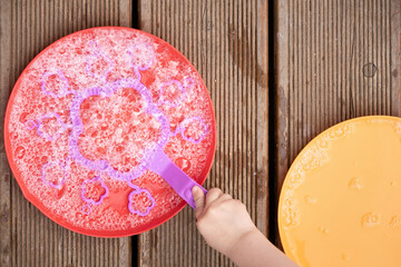 Fototapeta na wymiar Close-up of child's hands with bowl and bubble blower against wooden table or backdrop