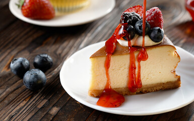 Strawberry topping pouring on fresh slice of cheesecake with blueberries, sweet and natural product, tasty baked dessert on wooden background, handmade pastry, appetizer bakery product in slow motion