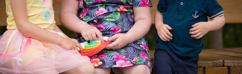 Girls playing with a rainbow pop it fidget toy. The push bubble fidget sensory toy is reusable silicone stress relief toy. Mental health concept. Motor skills development. Squeeze sensory game. Wide
