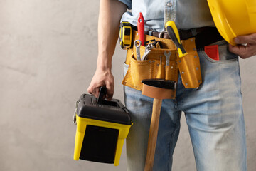 Man worker holding construction helmet and tool belt near wall. Male hand and construction tools