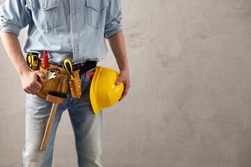 Man worker holding construction helmet and tool belt near wall. Male hand and construction tools - 440400795