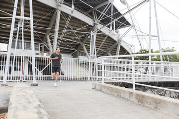 Young athlete asian man running in front of the stadium. The man trains outdoors. Preparing for the marathon.