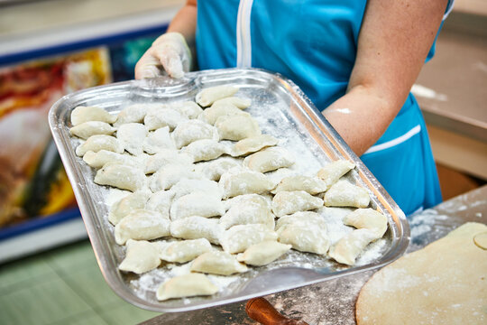 Woman's hands holding a tray full of dumplings sprinkled with flour . Delicious homemade food.