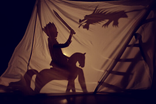 A fairy-tale shadow of a little prince on a horse with a sword and a dragon. Theatre. Childhood. Fairy tale.