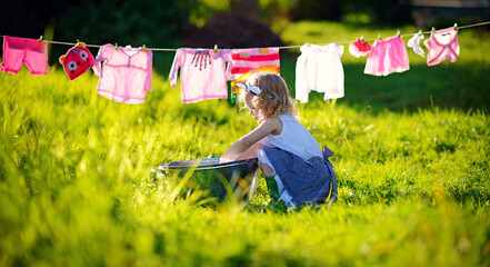 A little cute girl makes lingerie in a small aluminum pool near a clothing line in a meadow on a...