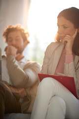 worried female with folder and cell phone in her lap, thinking, working from home with her colleague during coronavirus lockdown