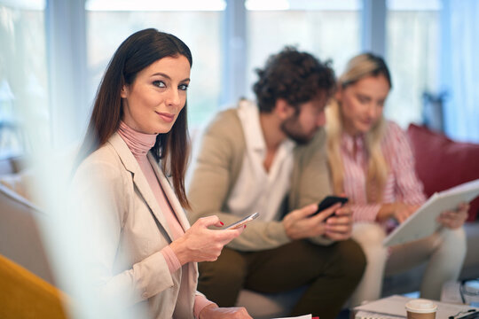 A young beautiful businesswoman texting and posing for a photo at a meeting with her colleagues. People, business, meeting