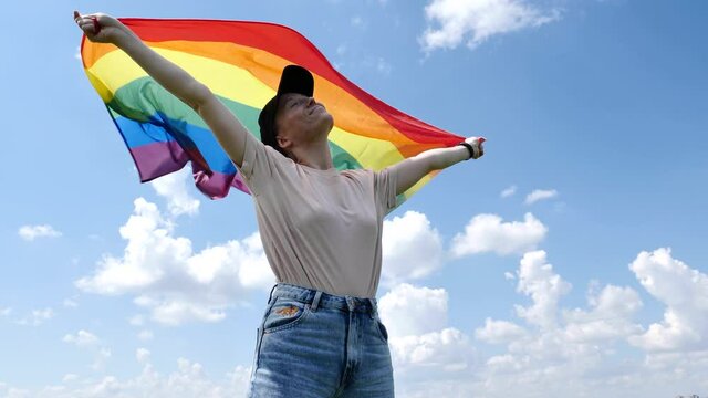Homosexual woman, Bisexual, girl, lesbian holding in hand a rainbow LGBT gender identity flag on sky cloudy background on a sunny, windy, summer day and celebrating a gay parade in pride month