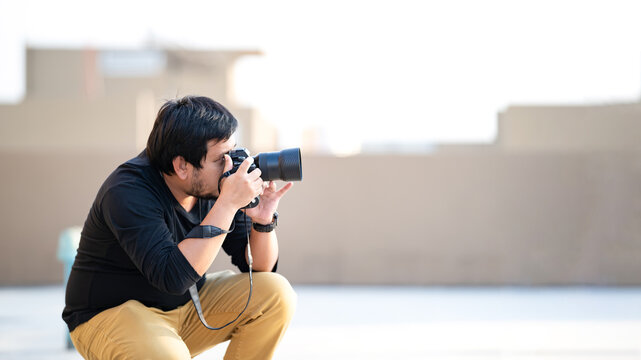 Asian Professional Camera man looks in to camera viewfinder and focus on the view for take a photo at rooftop outdoor field.