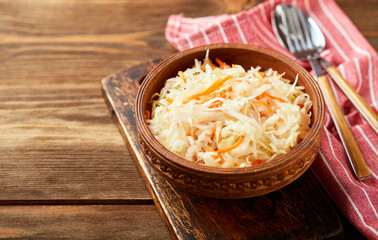 Sauerkraut, fermented cabbage with carrots in bowl on wooden background with copy space.