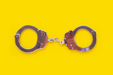 Metal handcuffs on yellow background