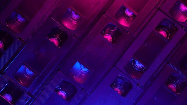 Retrofuturistic background of real VHS cassette pattern sliding to the right under blue and purple lighting, top view