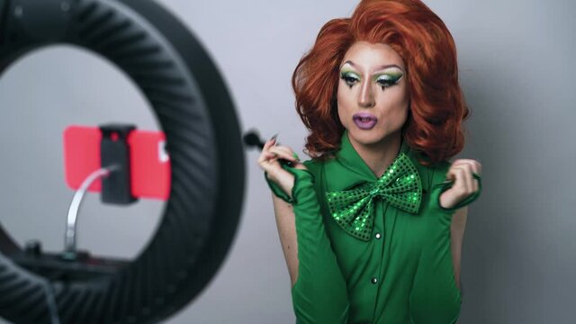 Happy drag queen social influencer vlogging online a makeup class with smartphone cam and ring led