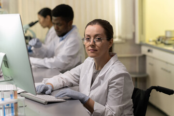 Fototapeta na wymiar Confident female chemist using computer by workplace against two colleagues