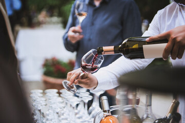 The waiter serves rose, red and white wine from the wine bottle in the wine glass at an event.