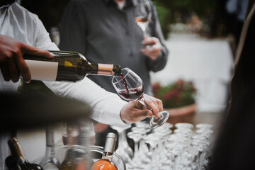 The waiter serves rose, red and white wine from the wine bottle in the wine glass at an event.