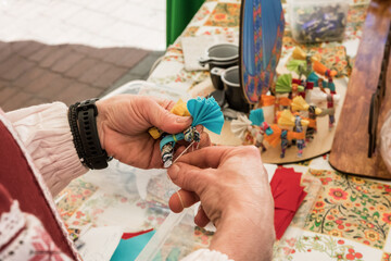 Master class on making handmade souvenirs. A woman makes a decorative doll-amulet.