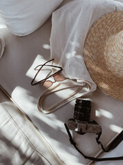 Female sunglasses, straw hat, shopper bag, retro photo camera on white lounge couch with pillows....