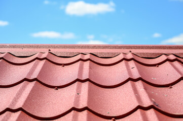 House roof. Red metal roof tiles. Roof made of metal sheets with cloudy sky in background.