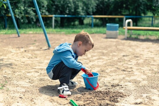 The boy pours sand into a bucket. Little boy plays in the playground