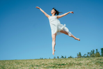 空と白いワンピースの踊る女性（ジャンプ）
