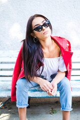 Beautiful young woman against white wall sitting on the bench