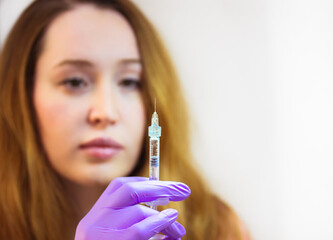 A young woman doctor wearing purple rubber gloves holds an injection syringe with a thin needle....