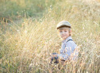 a sad offended boy sits in a field in the dry grass