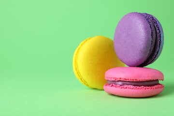 Delicious colorful macarons on green background, closeup. Space for text