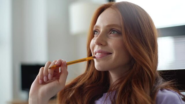 Close-up face of happy dreaming young woman making notes in paper notebook sitting on chair on background of window. Tracking shot of pretty lady writing down hopes and dreams of future into diary.