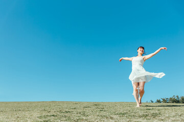 空と白いワンピースの踊る女性
