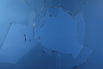 Closeup view of broken glass with cracks on blue background