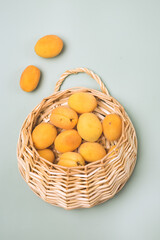 Delicious Ripe Apricots in Straw Basket on Light Green Background Top View Harvest Vertical