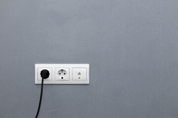 White sockets and black plug on gray wall. Plug connector, electricity and internet sockets.