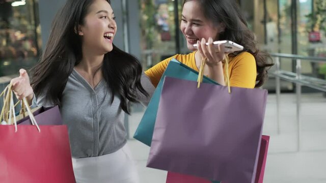 Smiling young Asian woman with shopping colour bags over mall background. using a smart phone shopping online  and smiling while standing mall building. lifestyle concept.slow motion 