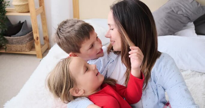 Loving mother kissing her children on bed at home