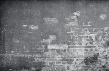 Front view of an old, dirty, damaged and plastered wall. Plaster is partly peeled off revealing old bricks. High resolution full frame textured background in black and white.