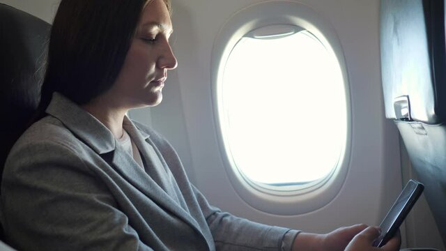 Brunette woman looking at the phone while sitting by the airplane window.