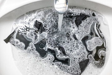 Black clothes lying in the water in the Water flowing down the drain in the washbasin ,covered with foam