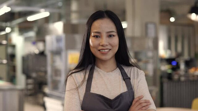 Asian woman smiling on camera while posing at own cafe